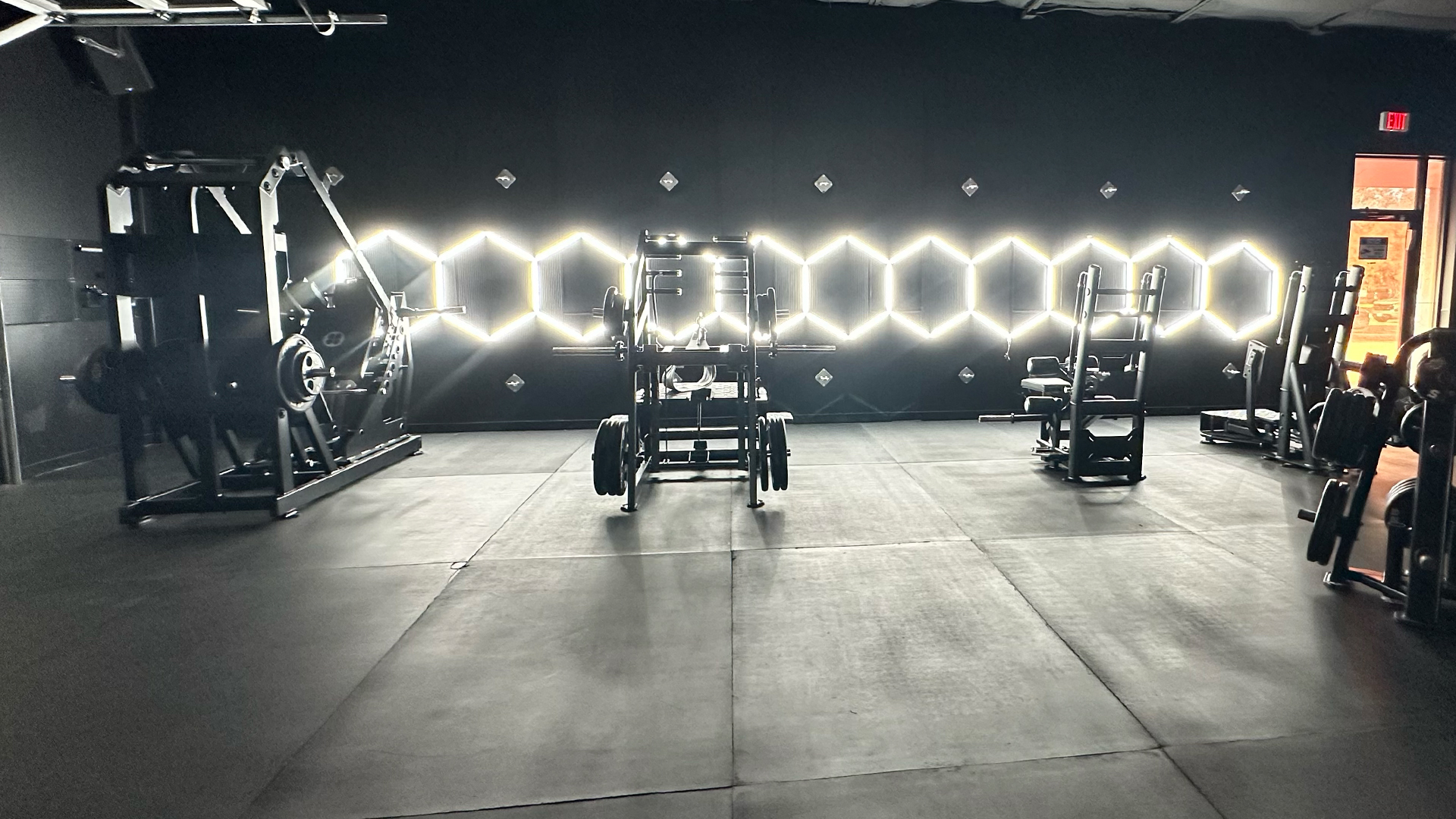 How Much Protein Do You Really Need for Glute Growth? What Studies Say 4 GluteZone hip thrust and strength machines installed in a modern dark gym with hexagon wall lighting