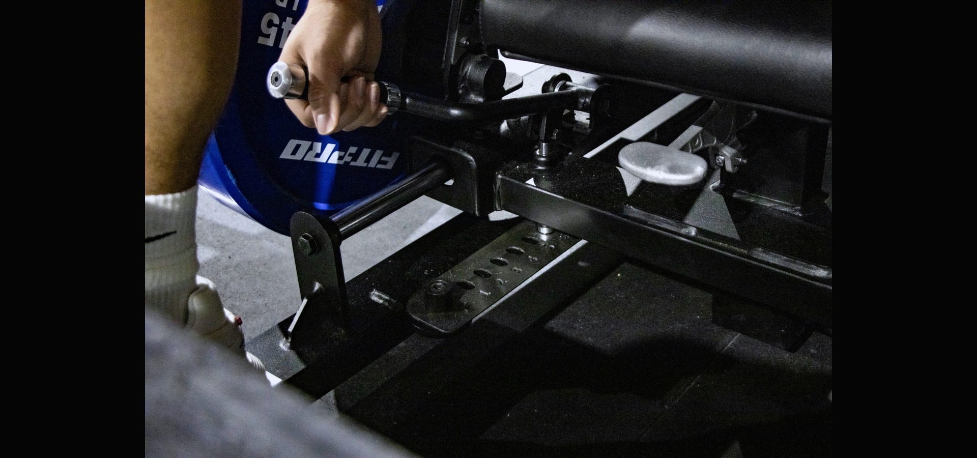 Close-up of a hand adjusting the seat rail on the GluteZone Hip Thrust Machine