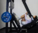 Woman training on a GluteZone Pendulum Squat machine in a bright studio, deep position with blue 45 lb plates.