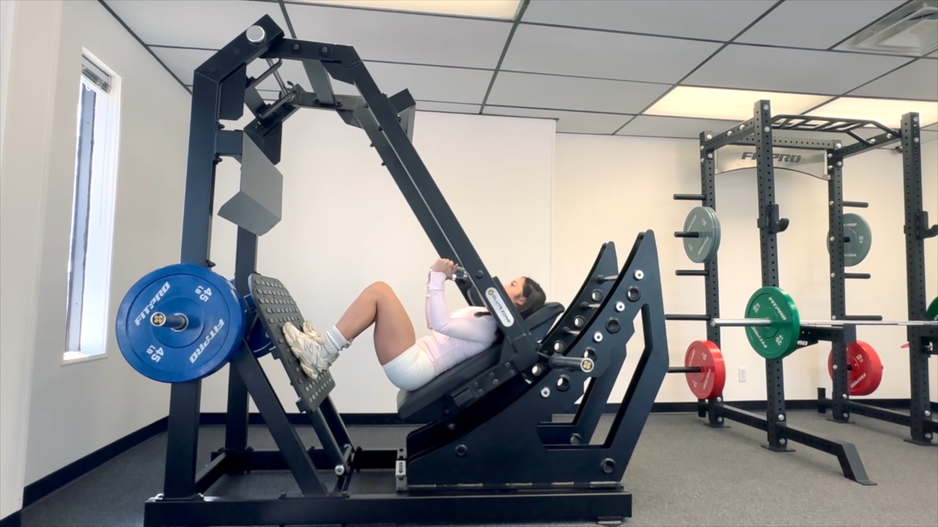 Mujer entrenando en una máquina Pendulum Squat de GluteZone en un showroom de gimnasio luminoso