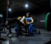 Woman seated on a GluteZone Hip Thrust Machine in a commercial gym, ready for a coached glute session.
