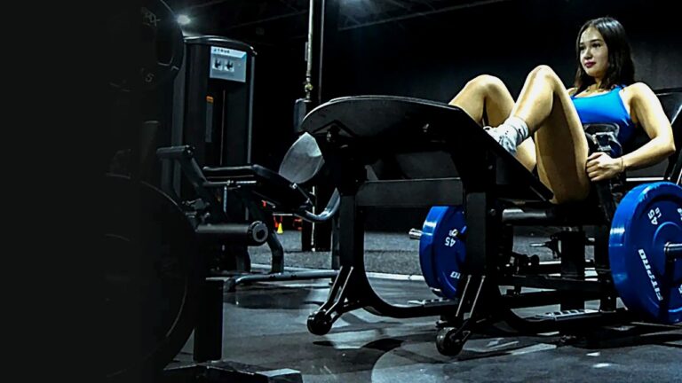 Woman performing a hip thrust on the GluteZone commercial hip thrust machine in a dark gym