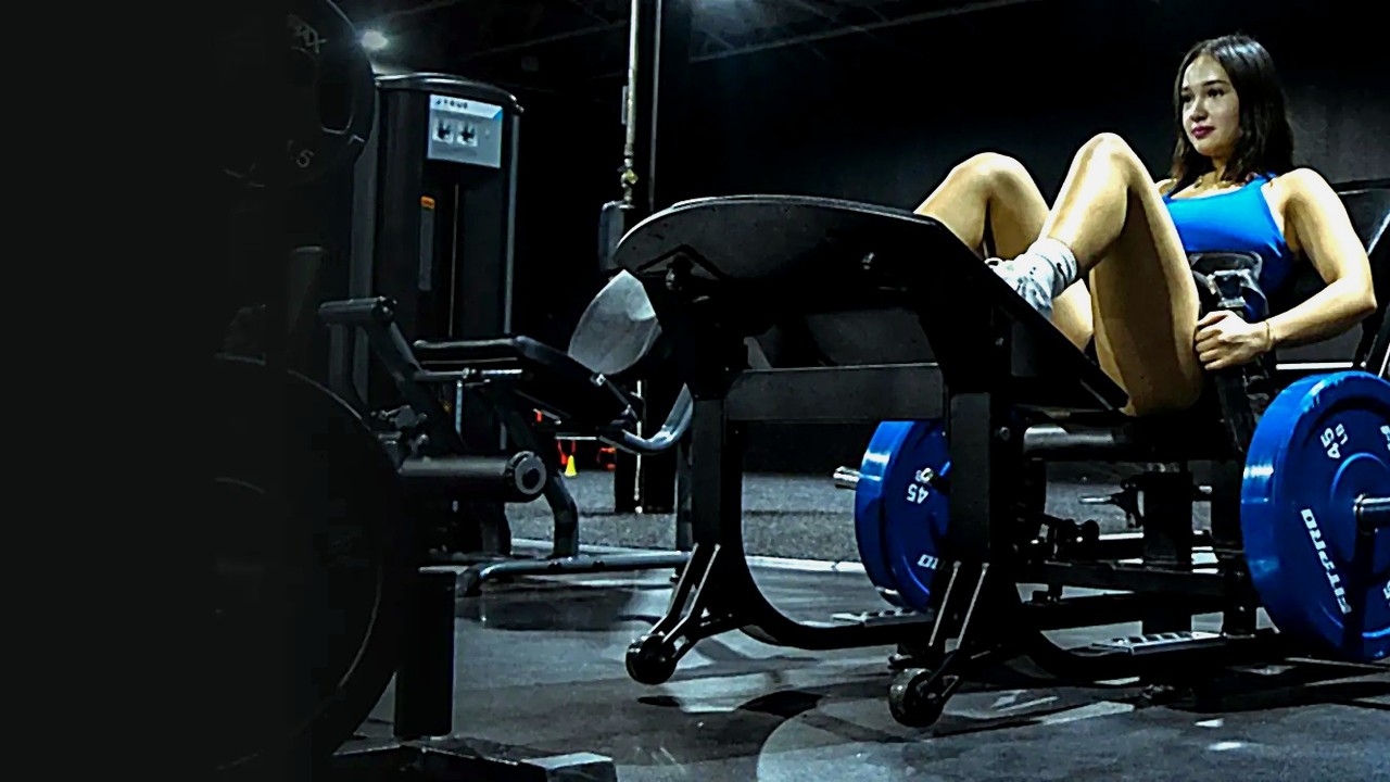 Woman performing a hip thrust on the GluteZone commercial hip thrust machine in a dark gym