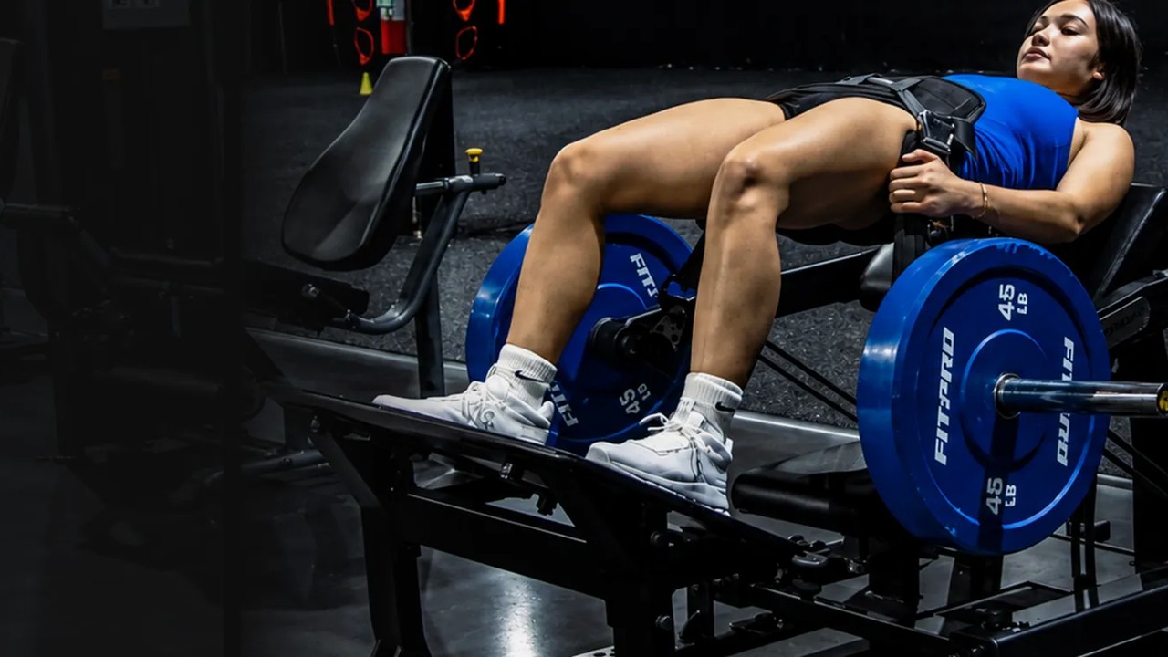 Mujer haciendo hip thrust en la máquina comercial de hip thrust de GluteZone en un gimnasio oscuro